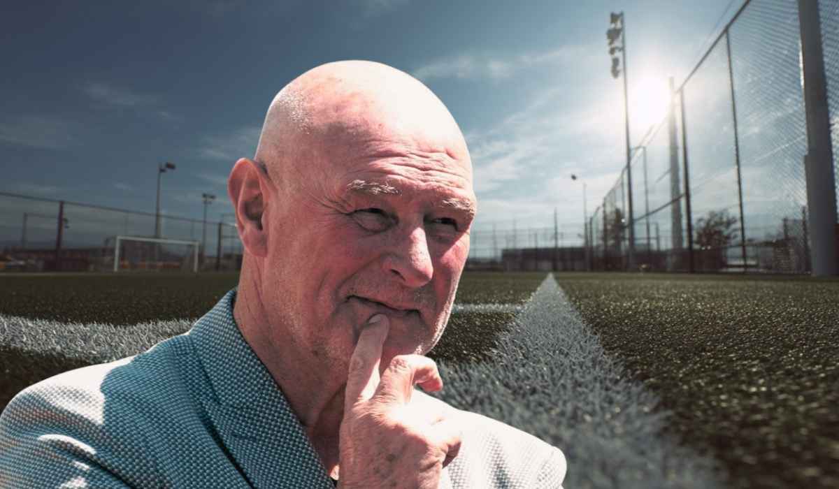 Älterer Mann steht nachdenklich am Rand eines Fußballfeldes